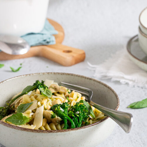 Pasta met pestoroomsaus, kip en broccoli op bord, met steelpan op de achtergrond