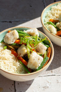 Wok met vis, gember en zwarte peper in twee kommen, zonlicht