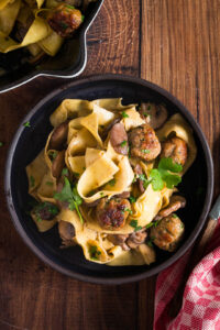 Pasta met gehaktballetjes en champignons op bord close-up, met de pan en een rode handdoek ernaast