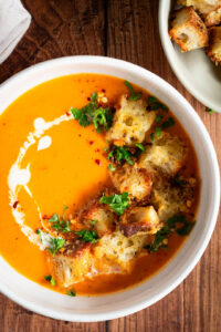 Soep van geroosterde pompoen met kaascroutons in een kom met peterselie, room en chilivlokken