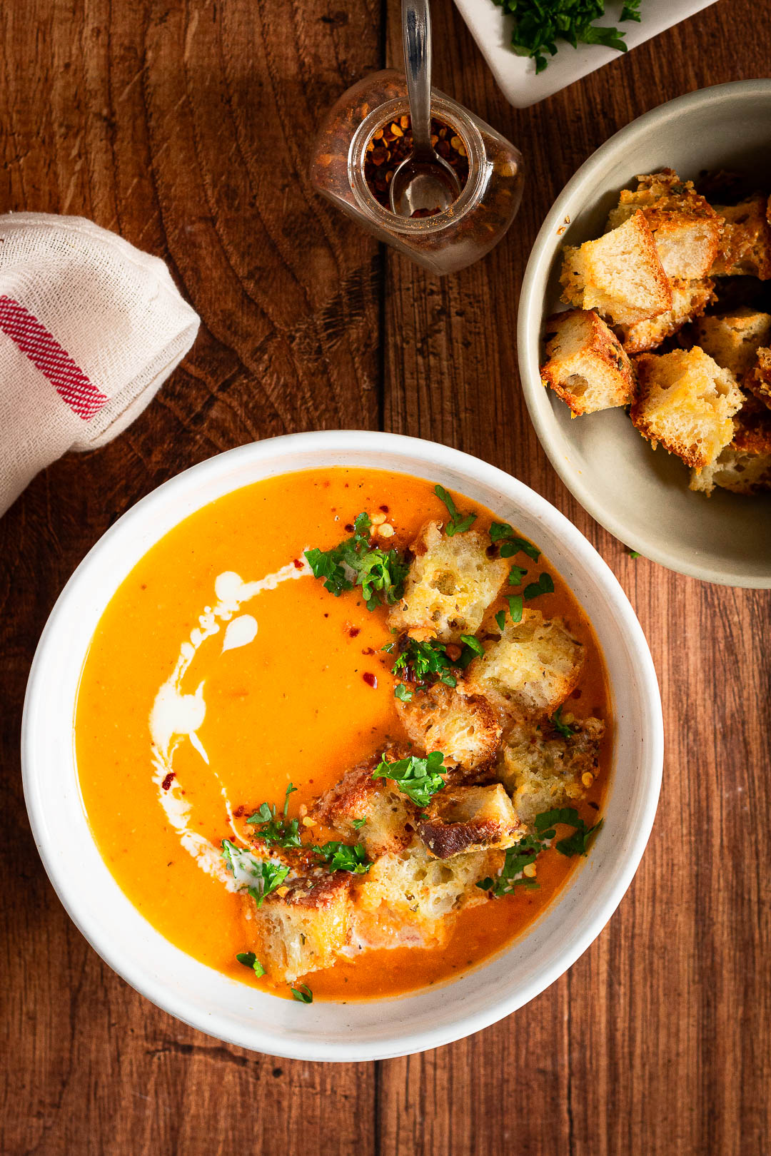 Soep van geroosterde pompoen met kaascroutons, met een kommetje croutons, peterselie en chilivlokken erbij