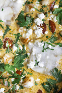Eenpansgerecht met vis en scampi-close up met feta en peterselie eroverheen gestrooid