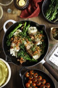 Kabeljauwhaasje in parmaham met sauce vierge en parmezaanpuree bovenaanzicht op tafel met gepofte tomaten en gestoomde bimi erbij