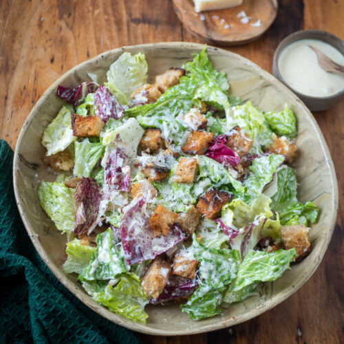 Caesar salad zoals het hoort, met een stuk parmezaan en wat dressing erbij op tafel.
